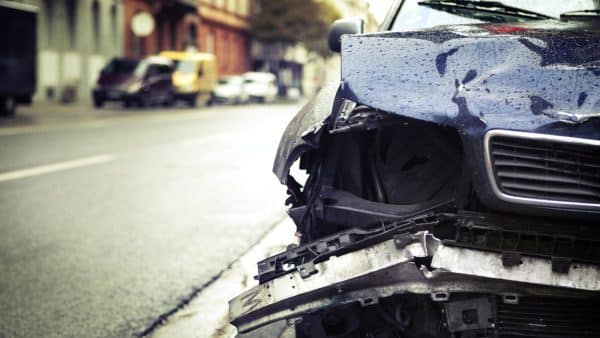 Crashed car with severe front-end damage on the side of a city street.